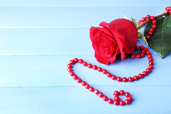 Όμορφο κόκκινο τριαντάφυλλο με χάντρες σε χρώμα φόντο ξύλινες σανίδες — Φωτογραφία Αρχείου