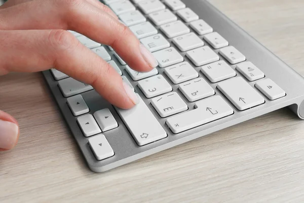 Main féminine avec clavier sur fond de bureau en bois — Photo