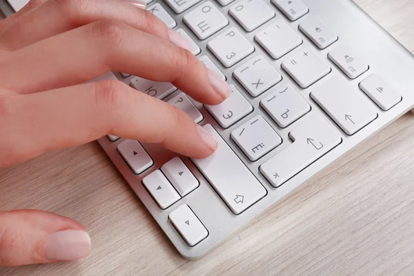 Main féminine avec clavier sur fond de bureau en bois — Photo