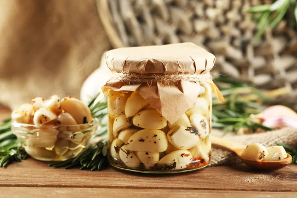 Canned garlic in glass jar, wicker mat and rosemary branches  on wooden background — Stock Photo, Image