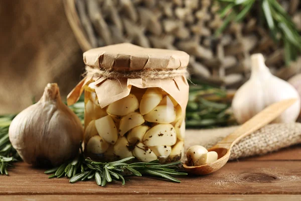 Konserverad vitlök i glas burk, wicker matta och rosmarin grenar på trä bakgrund — Stockfoto