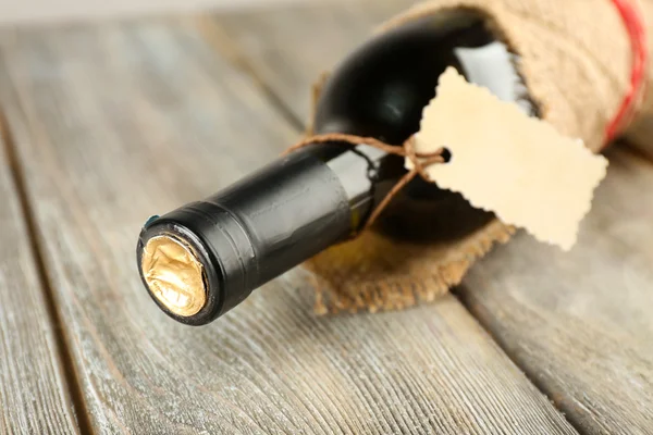 Garrafa de vinho envolto em pano de serapilheira em pranchas de madeira fundo — Fotografia de Stock