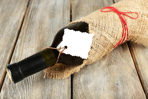 Bouteille de vin enveloppée dans un tissu de toile de jute sur des planches en bois — Photo