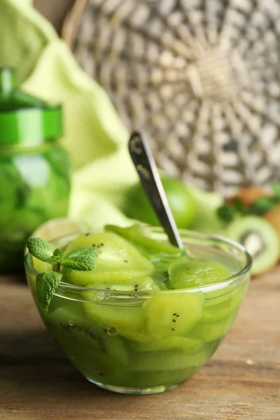 Smakelijke kiwi jam in glazen kom en jar op houten tafel, op rieten mat achtergrond — Stockfoto