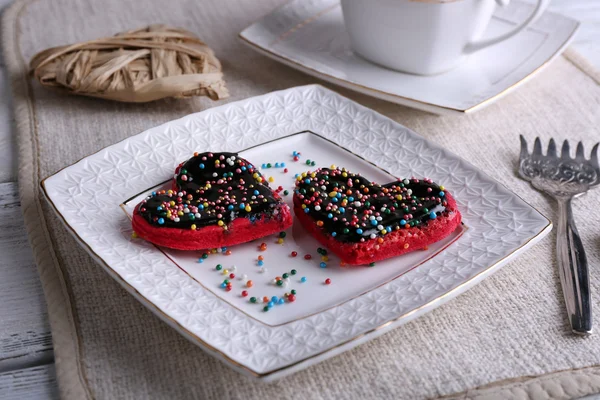 Biscoitos em forma de coração na placa e guardanapo, na cor de fundo de mesa de madeira — Fotografia de Stock