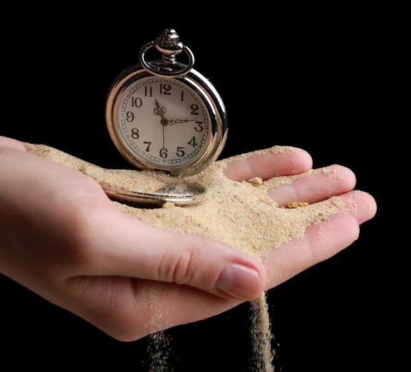 Reloj de bolsillo de plata en las manos y la arena que fluye sobre fondo negro — Foto de Stock