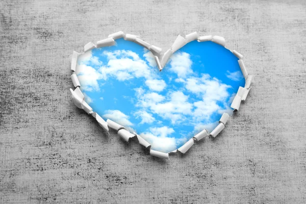 Blauwe hemelachtergrond met wolken door hartvormige gat in papier — Stockfoto