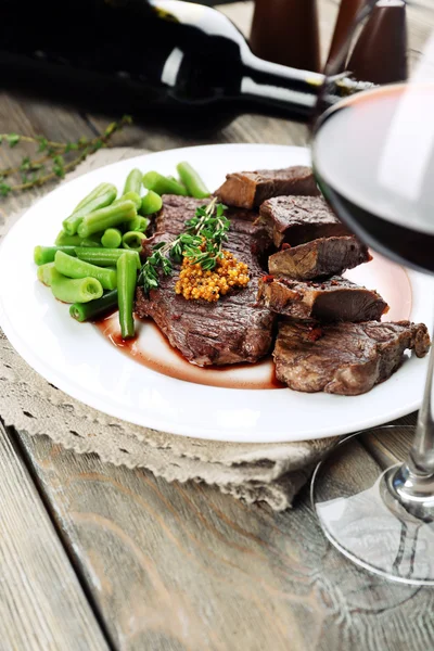 Steak on plate with bottle of wine on wooden background — Stock Photo, Image