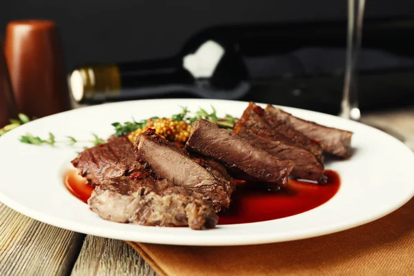 Steak with wine sauce on plate and bottle of wine on dark background — Stock Photo, Image