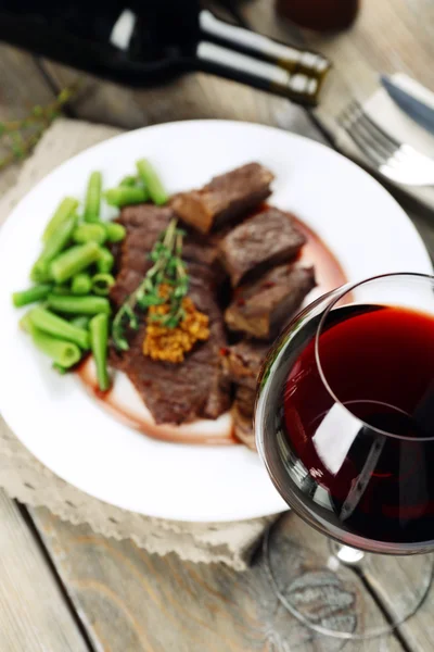 Bife na placa com garrafa de vinho em fundo de madeira — Fotografia de Stock