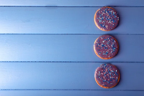 Three round glazed cookies on color wooden planks background