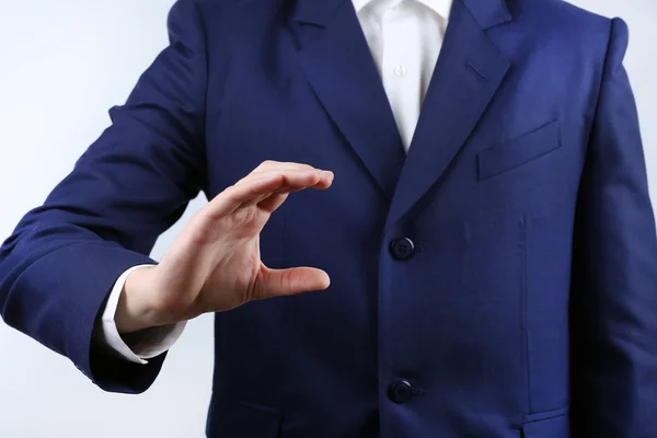 Empresario mostrando cualquier cosa sobre fondo gris — Foto de Stock