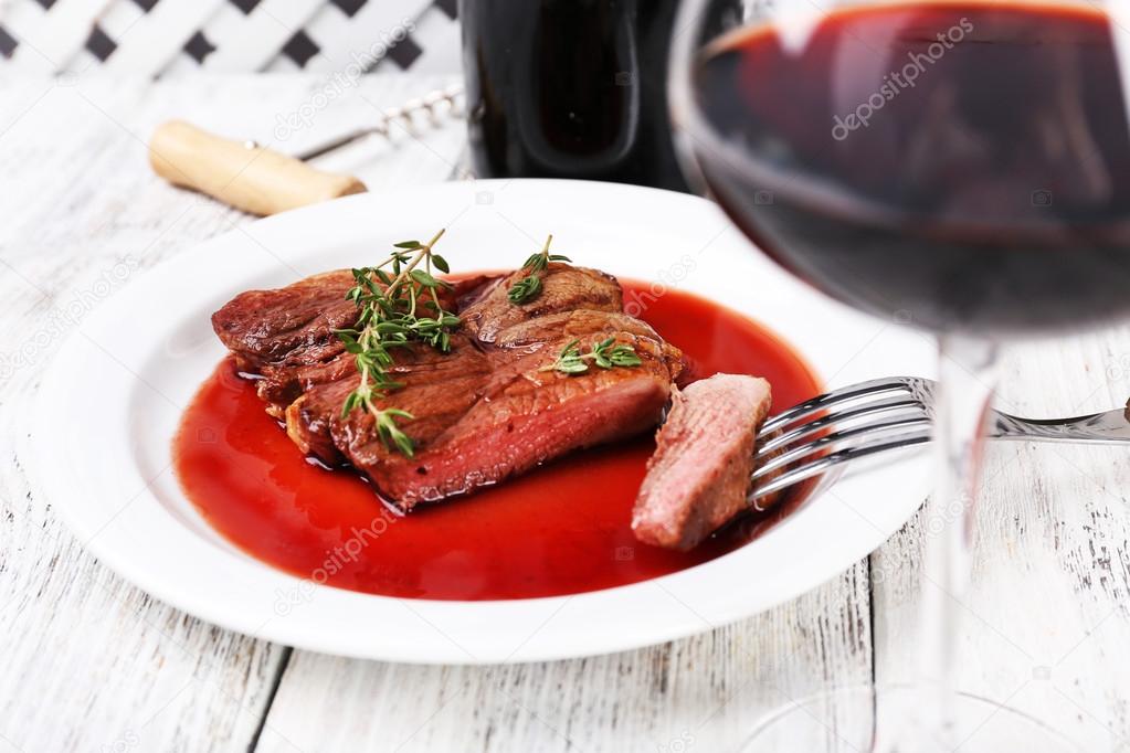 Steak with wine sauce on plate with bottle of wine on wooden background