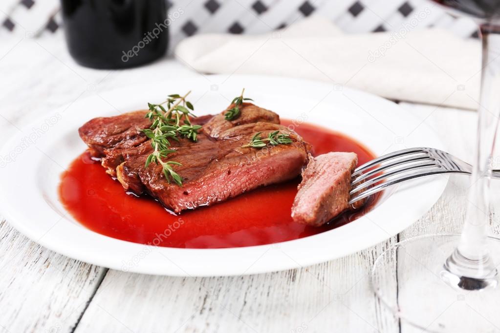 Steak with wine sauce on plate on wooden table