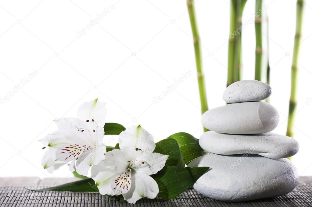 Still life of spa stones on bamboo mat surface with bamboo sticks isolated on white