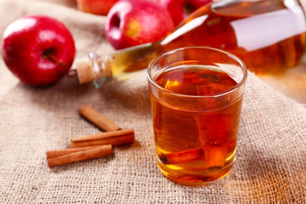 Apple cider met kaneelstokjes en verse appelen op zak achtergrond — Stockfoto