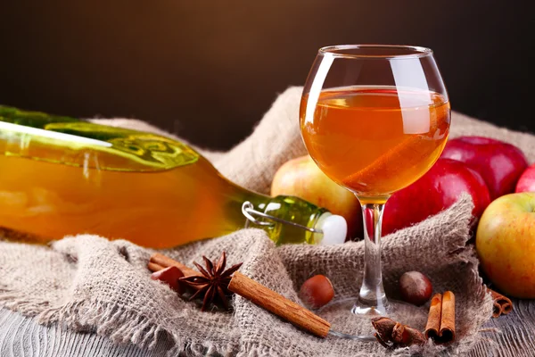 Sidra de manzana en copa de vino y botella, con palitos de canela y manzanas frescas sobre la mesa, sobre fondo oscuro — Foto de Stock