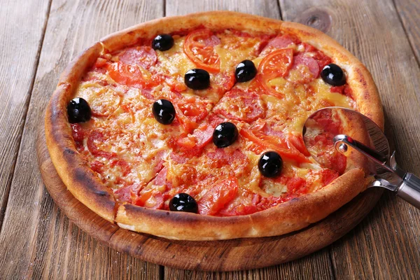 Pizza saborosa com azeitonas pretas e faca redonda a bordo e fundo de mesa de madeira — Fotografia de Stock