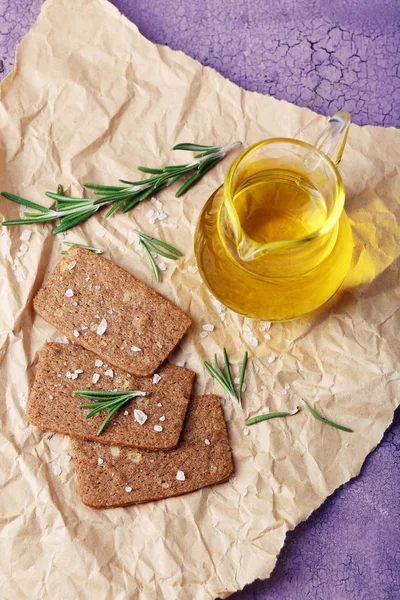 Pan crujiente con sal, jarra de aceite y ramitas de romero sobre papel arrugado y fondo de madera de color — Foto de Stock