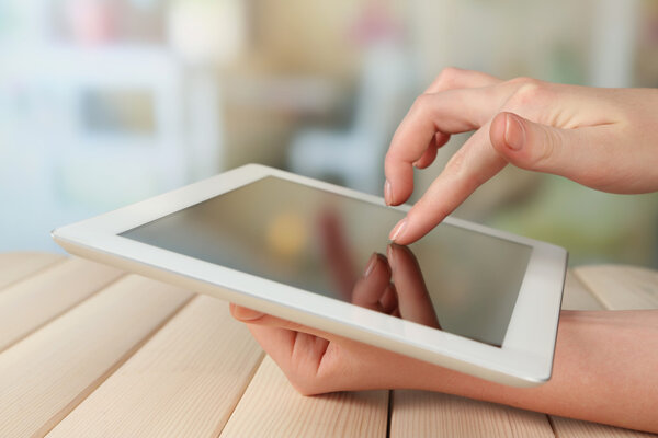 Hand using tablet PC on wooden table and light blurred background