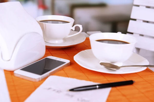 Dos tazas de café con bolígrafo y número de teléfono en servilleta en la mesa con alfombra de bambú naranja, sobre fondo claro — Foto de Stock