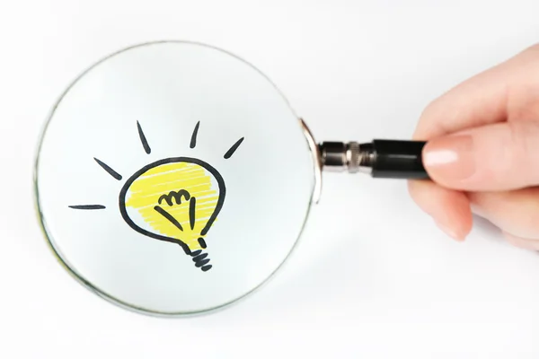 Symbol of idea as light bulb on sheet of paper through magnifying glass, on white background — Stock Photo, Image