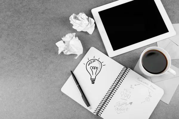 Symbol of idea as light bulb in notebook with crumpled paper, tablet and cup of coffee on wooden desk background — Stock Photo, Image