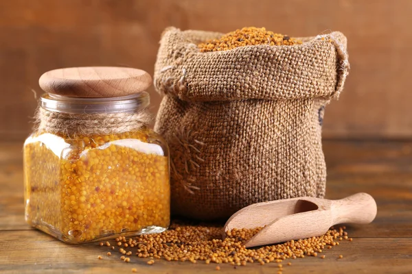 Mustard seeds in bag and Dijon mustard in glass jar on wooden background — Stock Photo, Image