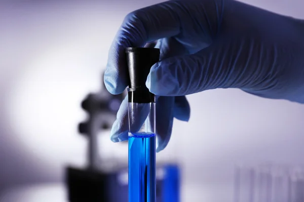 Laboratoriumglaswerk met blauwe vloeistof in hand van wetenschapper op grijze achtergrond — Stockfoto