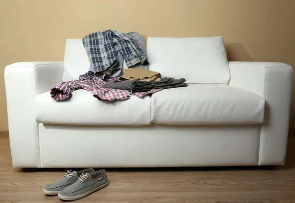 Ropa colorida en sofá blanco y zapatos masculinos en fondo de pared claro — Foto de Stock