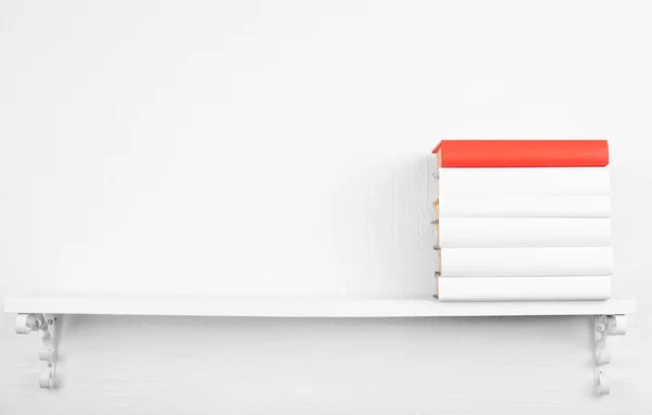 Blank books with red one on bookshelf on white wall background — Stock Photo, Image