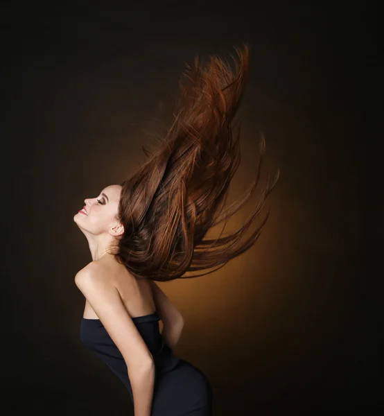 Mooie dansende jonge vrouw met stromen lange haren op donkere bruine achtergrond — Stockfoto