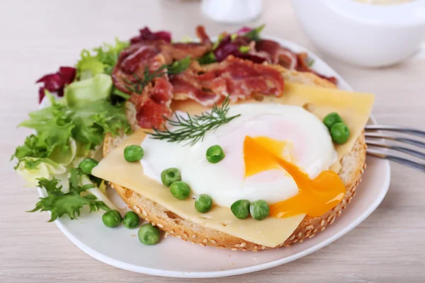 Sandwich con uova in camicia, formaggio e pancetta su piatto su fondo di legno — Foto Stock