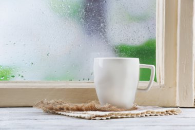 Yağmur arka plan pencere kenarında peçeteye ile sıcak içecek fincan