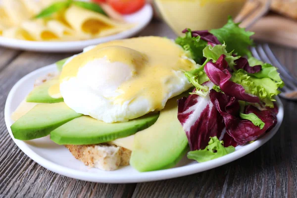 Toast with egg Benedict and avocado on plate on wooden table — Stock Photo, Image