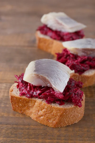 Herring with beets on rye toasts on wooden background — Stock Photo, Image