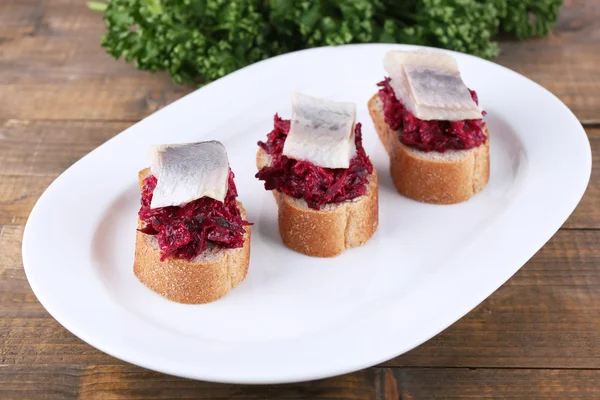 Rye toasts with herring and beets on plate on wooden background — Stock Photo, Image
