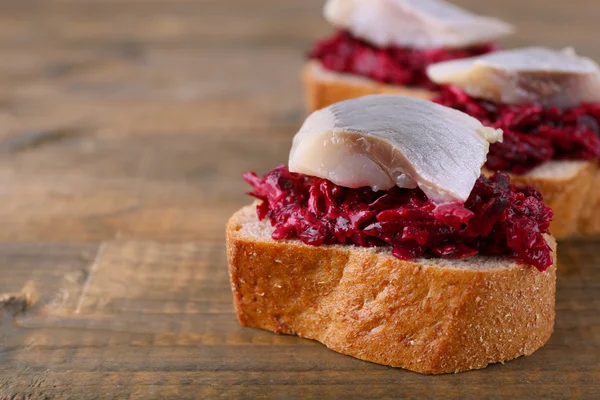 Herring with beets on rye toasts on wooden background — Stock Photo, Image