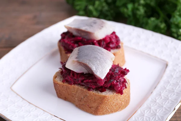 Rye toasts with herring and beets on plate on wooden background — Stock Photo, Image