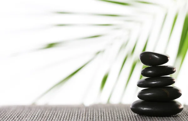 Stack of spa stones on bamboo mat surface with palm leaf isolated on white — Stock Photo, Image