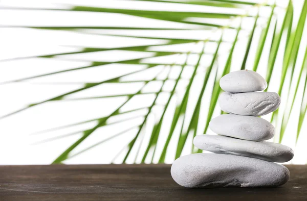 Natureza morta de pedras de spa em superfície de madeira com folha de palma isolada em branco — Fotografia de Stock