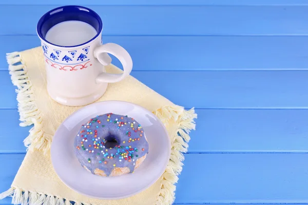 Donut vitrificado com xícara de leite em guardanapo e cor pranchas de madeira fundo — Fotografia de Stock