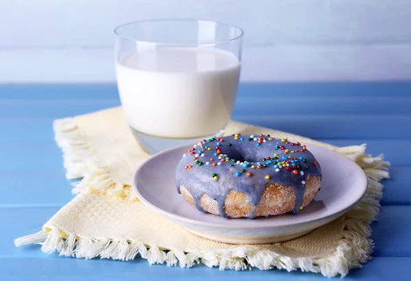 Glazed donut with glass of milk on napkin and color wooden background — Stock Photo, Image