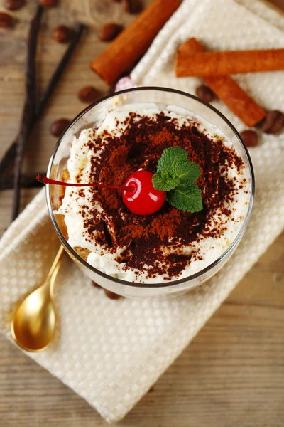 Sabroso postre tiramisú en vaso, en servilleta, sobre fondo de madera —  Fotos de Stock