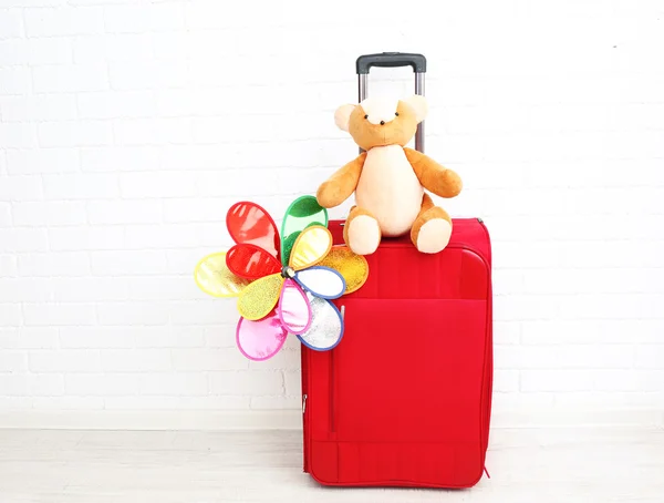 Red suitcase with toy flower and teddy bear on white brick wall background — Stock Photo, Image