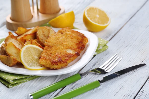 Filetto di pesce fritto impanato e patate con limone affettato sul piatto con tovagliolo su sfondo di tavole di legno di colore — Foto Stock