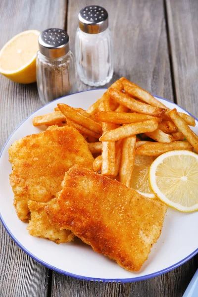 Filetes de peixe frito empanado e batatas com limão fatiado e talheres no prato e pranchas de madeira fundo — Fotografia de Stock