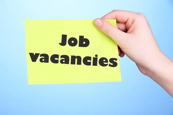 Job Vacancies text on piece of paper in hand on blue background — Stock Photo, Image