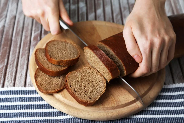 Mani femminili taglio del pane su tavola di legno, primo piano — Foto Stock