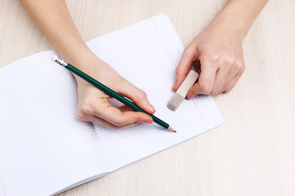 Manos humanas con lápiz escrito sobre papel y goma de borrar sobre fondo de mesa de madera — Foto de Stock